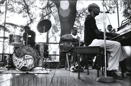 Professor Longhair sits at a piano on stage with his dreamy and bass player