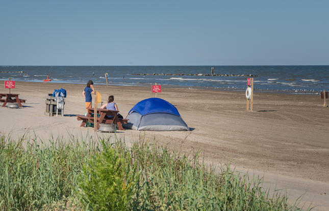 A family relaxes on a wooden bench outside a blue camping tent at Grand Isle State Park.