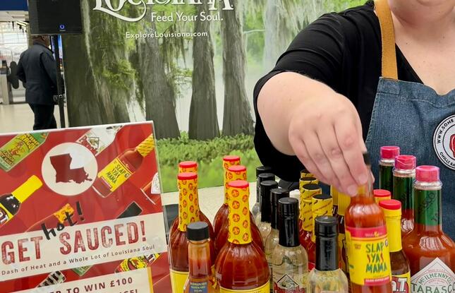 A woman reaches across a display of Louisiana hot sauces, which includes TABASCO, Louisiana brand and others.