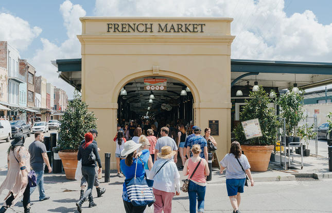A large archway making the entrance to the French Market in New Orleans, Louisiana, surrounded by people shopping.