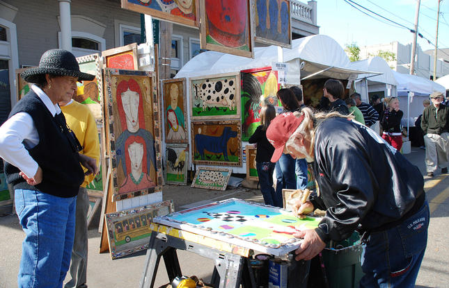 A woman with a large black hat watches a man paint at his booth at the Three Rivers Arts Festival in Covington.