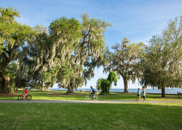 Two people ride bikes and two people jog along a paved trail on a sunny day at the Mandeville Lakefront. Credit: Louisiana Northshore