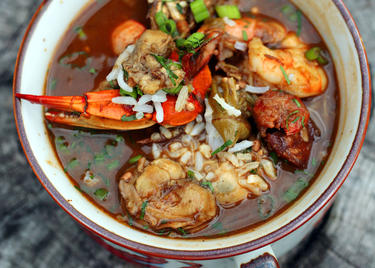 A red bowl piled high with seafood gumbo in a rich, tomato broth, with shrimp, crawfish and other seafood.
