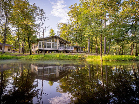 Chemin-A-Haut State Park cabins reflected in the water of the bayou and surrounded by bright green trees.
