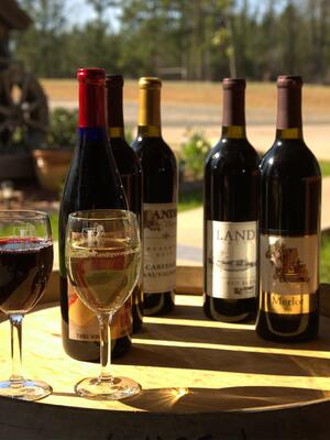 Bottles of red wine sit on a barrel behind a full glass of red wine and a full glass of white wine.