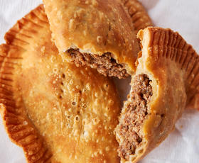 A perfectly fried, deliciously flaky meat pie, ripped in half to reveal buttery crust surrounding seasoned ground meat.