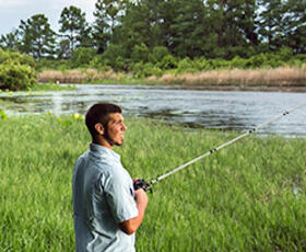 Man standing on the banks of a river holding a fishing rod