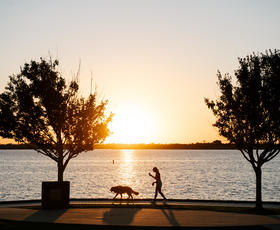 A person and their dog walk along Prien Lake at sunset.