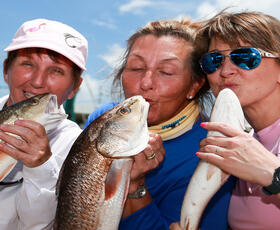 Three women holding fish and pretending to kiss them