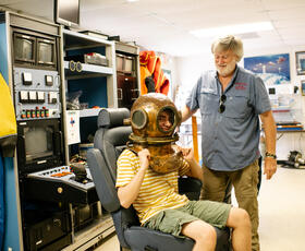 A child tries on a diver’s helmet under the watchful eye of an employee at the International Petroleum Museum and Exposition.