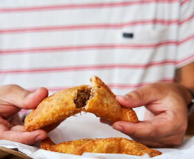 A person breaks open a golden-brown pastry filled with tender meat from Lasyone's Meat Pie Kitchen in Natchitoches, Louisiana.