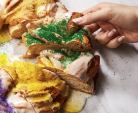 Someone grabs a slice of green-sprinkled king cake.