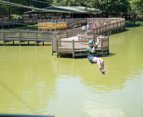 A child enjoys the zipline above light green water at Gators &amp; Friends.