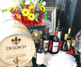 A wine display at CORK Wine Festival, featuring several bottles of red and white wine and a barrel advertising De Loach Vineyards.
