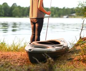 A person stands on the shoreline holding a fishing rod beside a kayak on calm water.