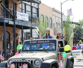 Two girls wearing crowns ride in a gray Jeep through the streets of downtown New Iberia during the Louisiana Sugar Cane Festival parade.