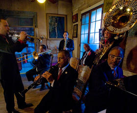 Jazz musicians in formal suits performing with various instruments inside the Preservation Hall in New Orleans, Louisiana.
