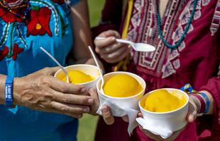 Hands hold three bright orange mango freezes at the New Orleans Jazz &amp; Heritage Festival.