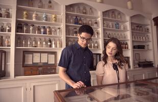 Two people examine medicinal artifacts at the New Orleans Pharmacy Museum, with a wall of bottles of various sizes and shapes behind them.