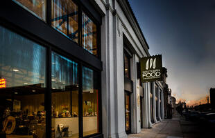 The exterior of the Southern Food &amp; Beverage Museum in New Orleans at night, warmly lit from interior lighting.